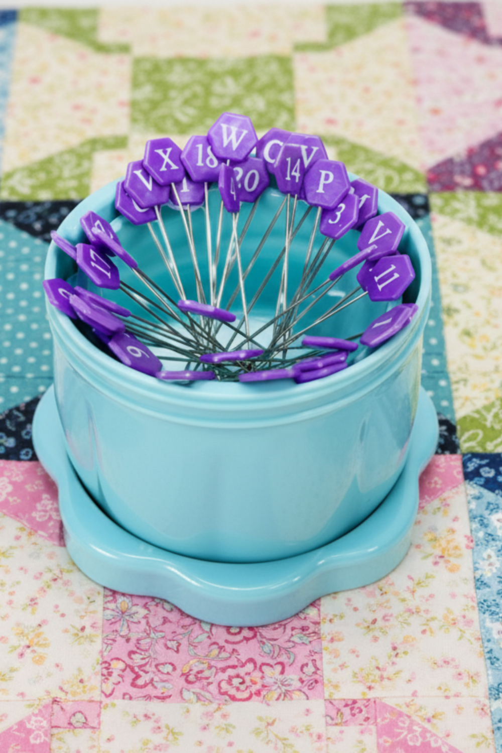 Taylor Seville alphabet pins in turquoise magnetic pin cup displayed on a colorful patchwork quilt