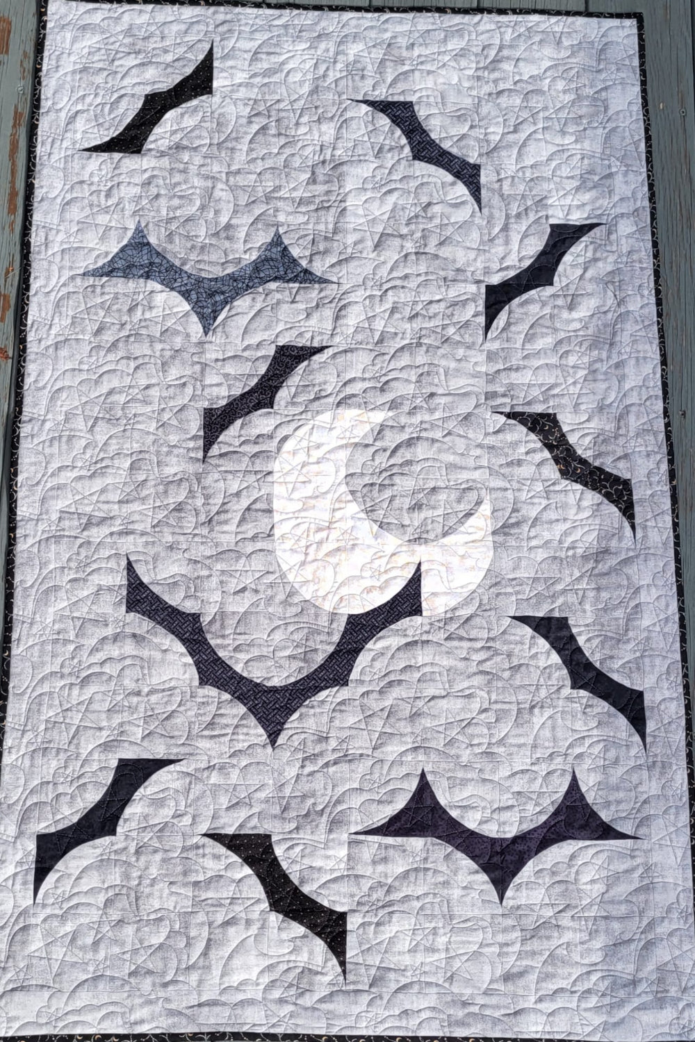 Handmade quilt with a light gray quilted background, dark bat shapes, and a cream crescent moon, finished with black binding.