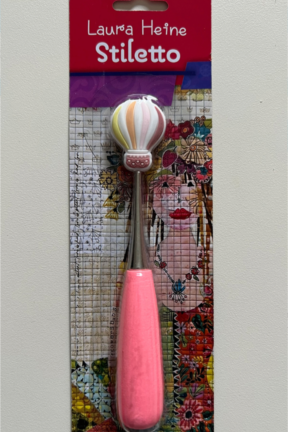 Close-up of Laura Heine Stiletto packaging showing hot-air balloon handle detail and collage artwork backing.