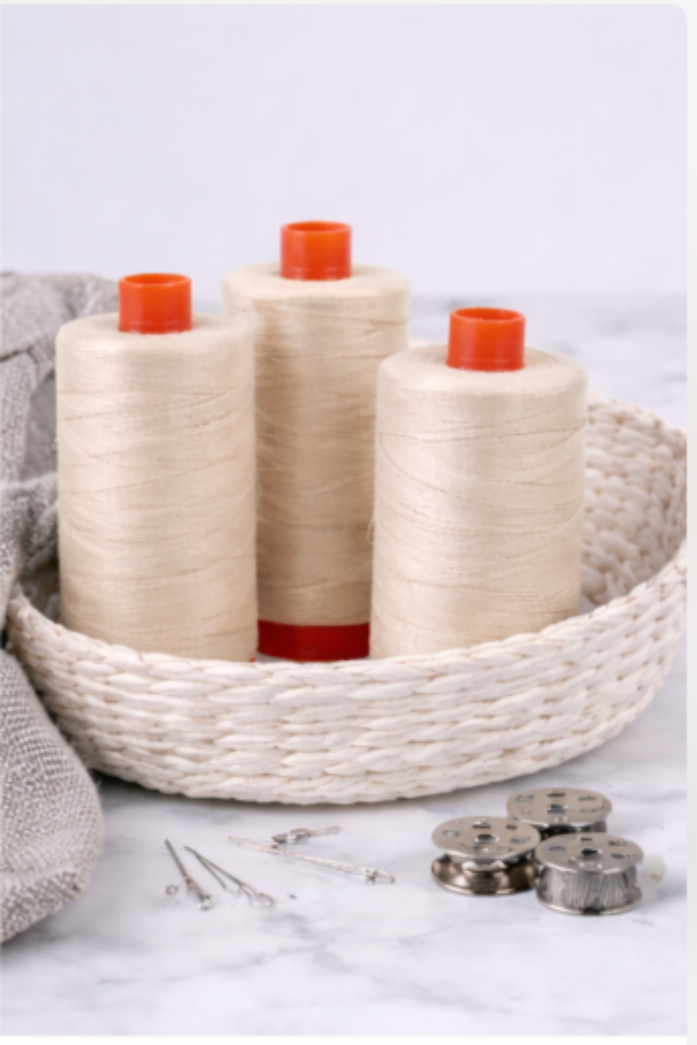 Three Aurifil Mako Cotton Thread 50wt Aluminum spools displayed in a woven basket with sewing accessories.