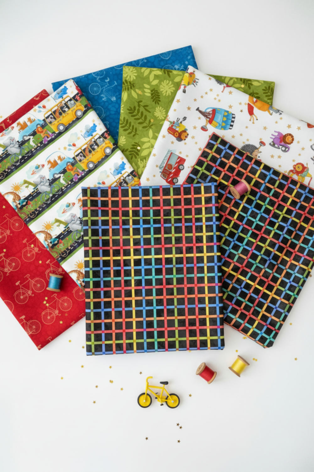 On the Go Plaid Multi quilting cotton by Jason Yenter for In The Beginning Fabrics — vertical Pinterest-style fan spread with the bold rainbow grid on black as the front hero fabric, with a yellow toy bicycle, gold star confetti, and colorful thread spools below. Coordinating fabrics and quilt patterns available at IraRobi Quilts.