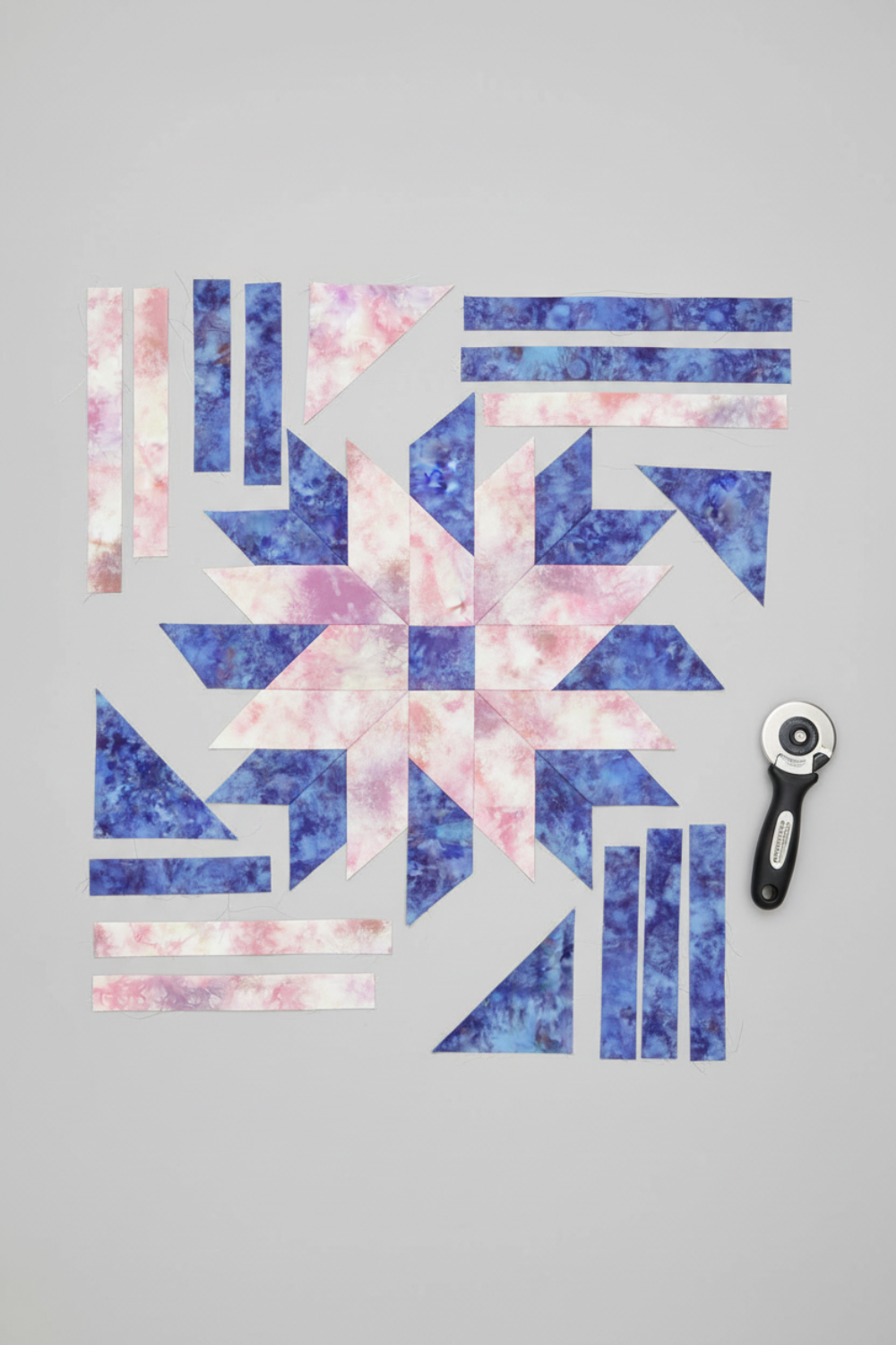 Fire & Ice by Maywood Studio Peach Ice Dye and coordinating cotton quilting fabric cut into quilt block pieces with a rotary cutter on light grey background