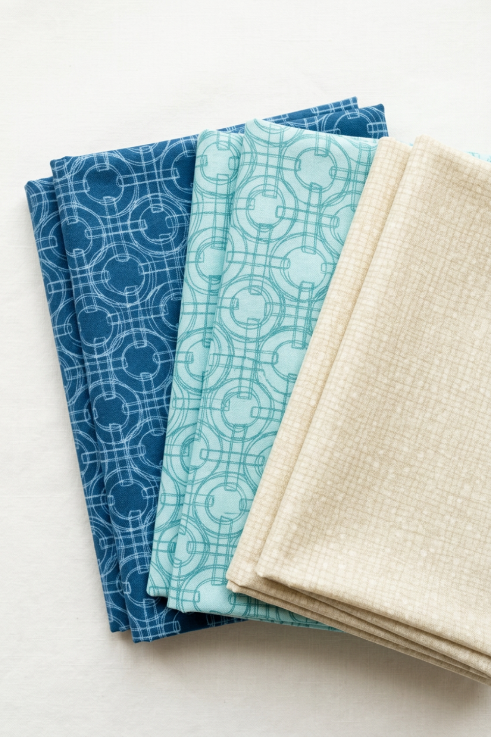 Folded Serena Shores Coastal and Mist fabrics by Robin Pickens for Moda Fabrics, with deep blue and pale aqua linked-ring prints alongside a coordinating cream textured fabric.
