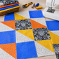 Safari Fun Floating Triangles White/Black by Terry Runyan for Benartex – in-progress quilt top featuring white with black triangle outlines as background fabric, paired with blue, orange, and gold quilting cottons, with sewing machine and rotary cutter on a wooden table