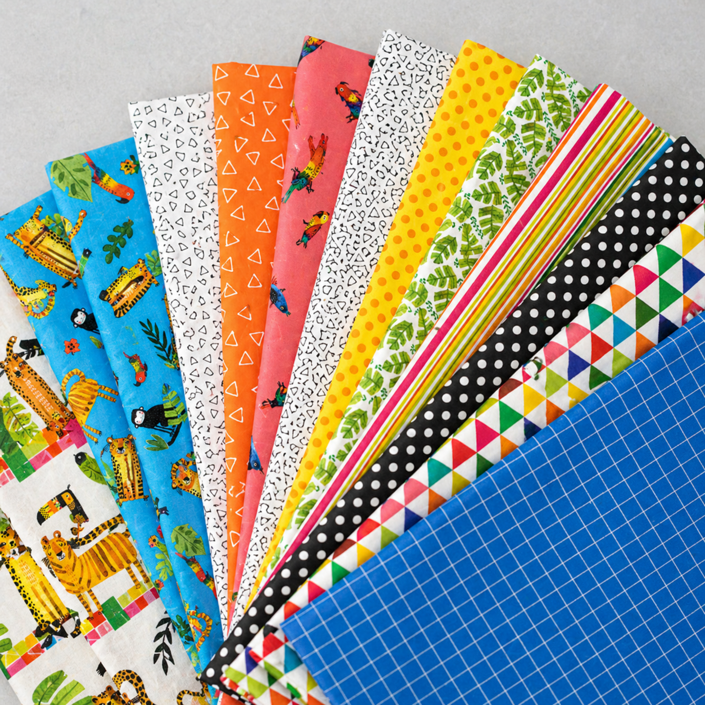 Safari Fun by Terry Runyan for Benartex fabric collection fanned out on light grey — coordinating quilting cottons including blue jungle animals, white/black floating triangles, orange floating triangles, coral parrot print, yellow orange dots, and green jungle leaves — IraRobi Quilts