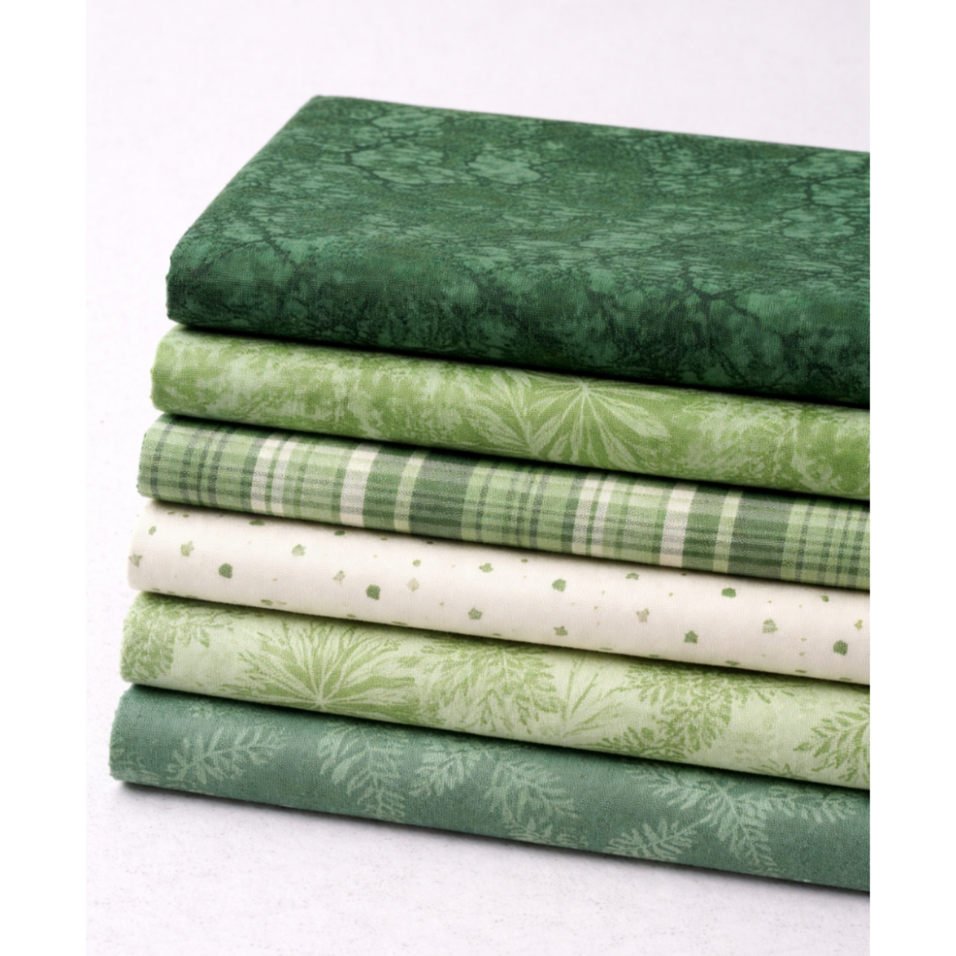 Expressions Batiks Hand-Dyes Evergreen fabric by Riley Blake Designs on top of a coordinating stack of green quilting cotton fabrics in a range of shades from deep forest green to soft sage, light plaid, cream with sage dots, and medium botanical green – rich deep forest green hand-dyed batik with organic mottled texture, 100% cotton batik
