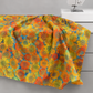 Impressions Gold Daisies quilting cotton fabric draped over a sewing table showing allover large-scale daisy pattern – vibrant golden yellow, orange, and red blooms on teal and blue watercolor ground by Jason Yenter for In The Beginning Fabrics, 100% cotton, 3 yard cut