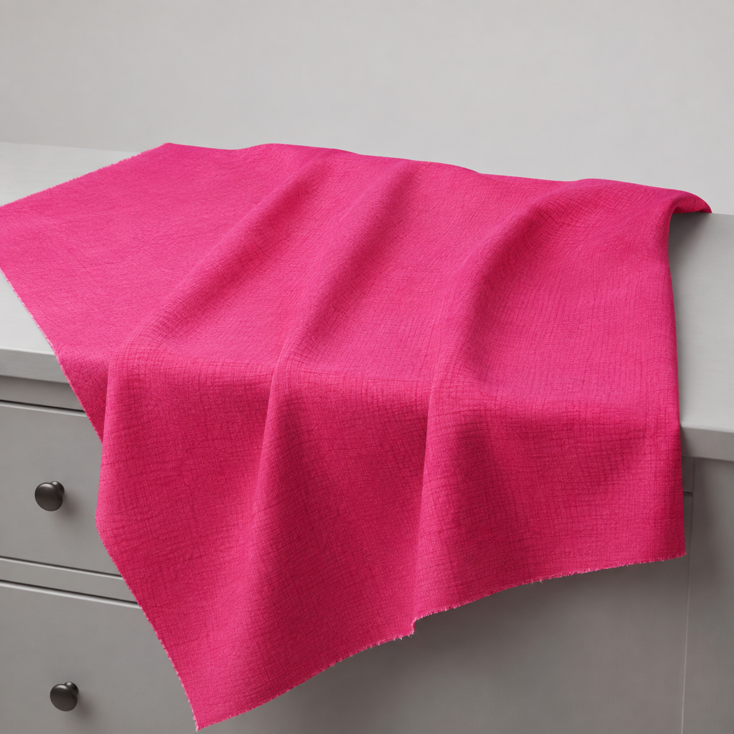 Thatched Fuchsia quilting cotton fabric by Robin Pickens for Moda Fabrics draped over a grey table edge with soft natural folds showing the vibrant fuchsia-hot pink tonal crosshatch texture and raw cut edges. Available at IraRobi Quilts.