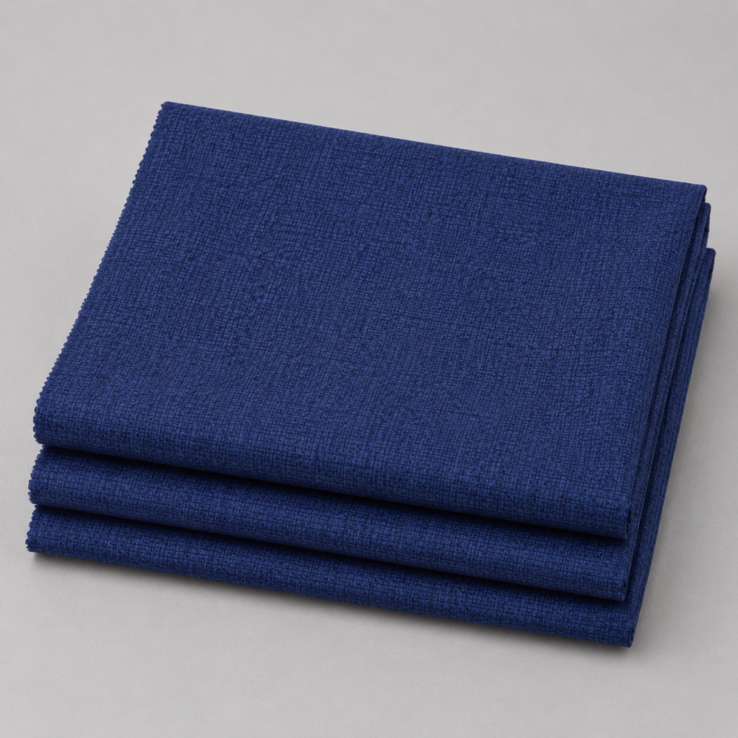 Thatched Navy quilting cotton fabric by Robin Pickens for Moda Fabrics neatly folded in a stack on a light grey surface showing the rich deep navy blue tonal crosshatch texture and raw cut edges. 100% cotton, 43–44" wide. Available at IraRobi Quilts.