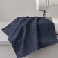 Dotty Thatched Indigo fabric by Robin Pickens for Moda Fabrics draped over a sewing machine with soft natural folds showing the deep indigo-charcoal ground with scattered tonal grey dots. Available at IraRobi Quilts.