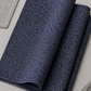 Dotty Thatched Indigo fabric by Robin Pickens for Moda Fabrics folded in a neat stack on a light grey surface with a cutting mat and rotary cutter — deep indigo-charcoal with scattered tonal grey dots. Coordinating fabrics and quilt patterns available at IraRobi Quilts.