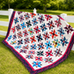 Triangles Galore finished quilt from Studio 180 Design displayed against white fence on green lawn — scrappy spinning triangle blocks in multicolor batiks including red, teal, blue, orange, and purple on white background with raspberry inner border and dark navy floral outer border — full size 82¾″×97″ made with Tucker Trimmer III tool