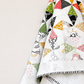 Dissolve quilt pattern by Zen Chic — close-up of FPP quilt hanging on wall showing bold geometric diamond and triangle fragments in red, green, gold, black and white Ampersand prints with whisper-white background and black-and-white striped binding — Dissolve pattern available at IraRobi Quilts