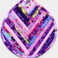 Leaf-Shaped Quilted Hot Pad – Violet Bloom, front view showing herringbone chevron strip piecing in deep violet, purple, lavender, pink, magenta, blue, and chartreuse prints with soft pink binding border and floral accent – handmade by IraRobi Quilts