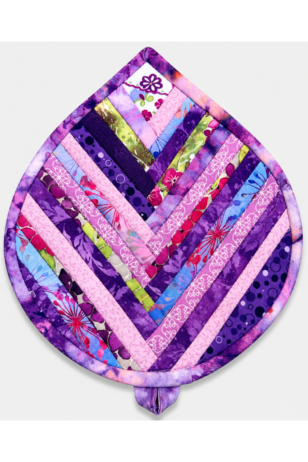 Leaf-Shaped Quilted Hot Pad – Violet Bloom, front view showing herringbone chevron strip piecing in deep violet, purple, lavender, pink, magenta, blue, and chartreuse prints with soft pink binding border and floral accent – handmade by IraRobi Quilts