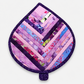 Leaf-Shaped Quilted Hot Pad – Lavender Garden, front view showing herringbone chevron strip piecing in lavender, pink, magenta, blue, and floral prints with deep purple dot-swirl border – handmade by IraRobi Quilts