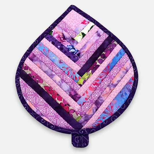 Leaf-Shaped Quilted Hot Pad – Lavender Garden, front view showing herringbone chevron strip piecing in lavender, pink, magenta, blue, and floral prints with deep purple dot-swirl border – handmade by IraRobi Quilts