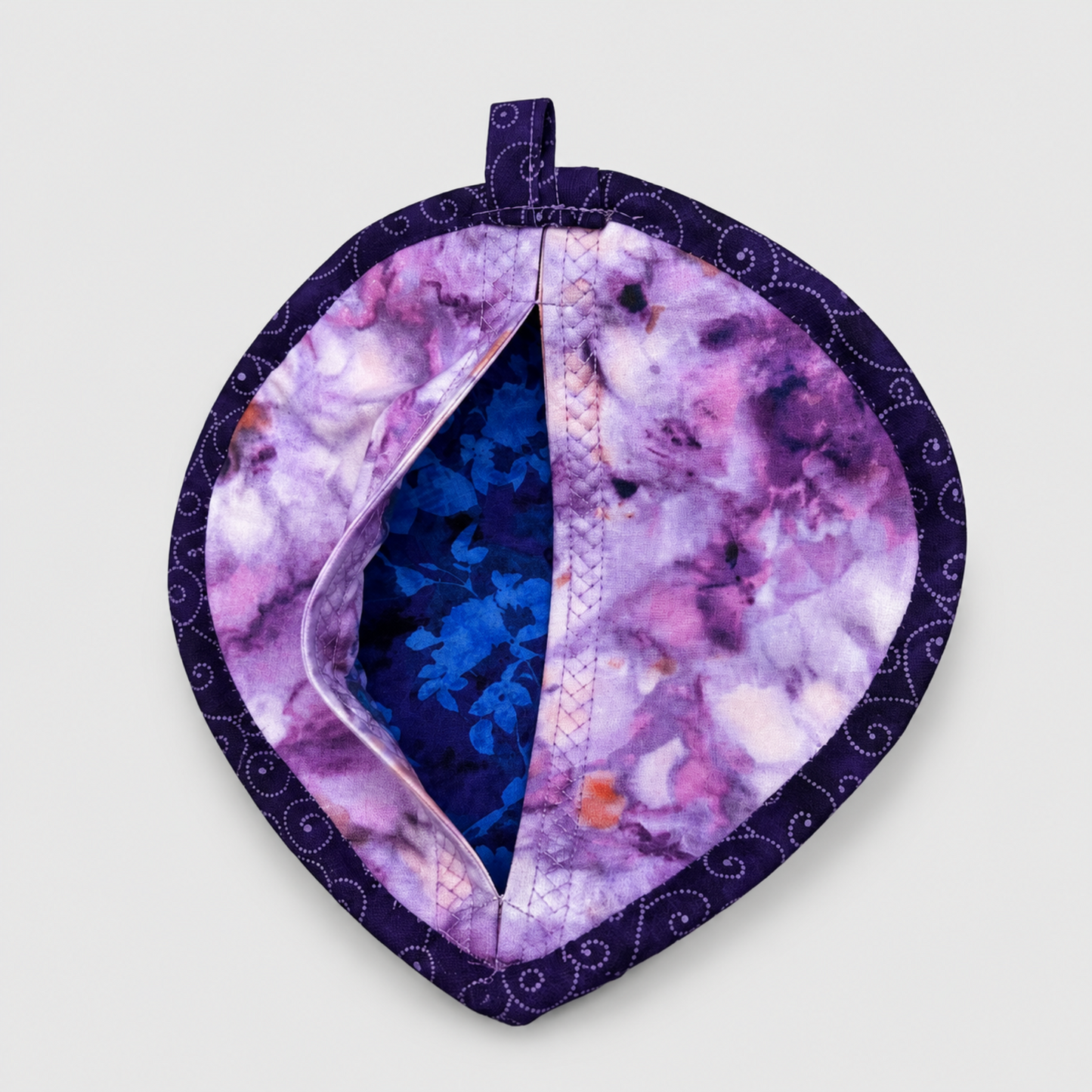 Leaf-Shaped Quilted Hot Pad – Lavender Garden, pocket open showing bright blue floral batik lining inside, with purple watercolor batik back and deep purple dot-swirl border – handmade by IraRobi Quilts