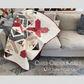 Criss Cross Kisses quilt by Robin Pickens draped over gray sofa showing X blocks and arrowhead details in crimson, navy and floral prints on cream background with red binding