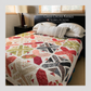 Criss Cross Kisses queen size quilt by Robin Pickens on bed showing full layout of X blocks and arrowhead sashing in pink, green, crimson, navy and floral prints on cream background with red binding