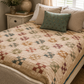 The Fox Homestead by Stacy West for Henry Glass — nine-patch pinwheel quilt on a vintage cane bed, pieced in dusty rose, sage, burgundy, and gold on a cream ditsy ground with a teal border, foot-of-bed view in a cottage bedroom