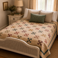 The Fox Homestead by Stacy West for Henry Glass — nine-patch pinwheel quilt on a vintage cane bed in a cottage bedroom, pieced in dusty rose, sage, burgundy, and gold on a cream ditsy ground with a teal border, styled with a sage floral pillow