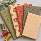 The Fox Homestead fabric collection by Stacy West for Henry Glass — five coordinating quilting cottons fanned out including sage green floral vine, cream daisy clusters, rust leaves and berries, slate green tumbling cubes, and cream sand paisley swirl, with wooden thread spools