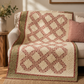 The Fox Homestead fabrics by Stacy West for Henry Glass showcased in the Kelley ocean wave quilt pattern by Edyta Sitar of Laundry Basket Quilts — dusty rose, cream, and burgundy with sage green border, draped over a cream sofa