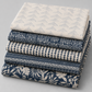 Coordinating quilting cottons from the Breezeway collection by Maywood Studio — neatly stacked folds of cream/grey chevron, navy geometric tile, cream/navy mini triangles, navy tribal stripe, and navy tropical palm and monstera silhouette prints, 100% cotton 43–44" wide