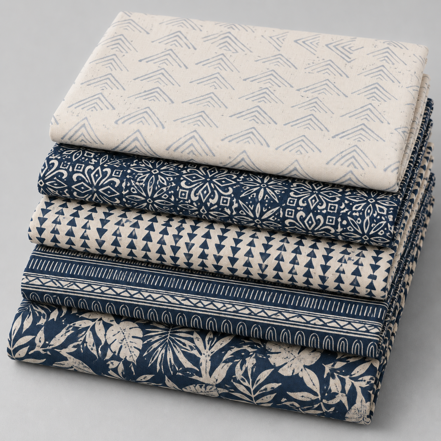 Coordinating quilting cottons from the Breezeway collection by Maywood Studio — neatly stacked folds of cream/grey chevron, navy geometric tile, cream/navy mini triangles, navy tribal stripe, and navy tropical palm and monstera silhouette prints, 100% cotton 43–44" wide