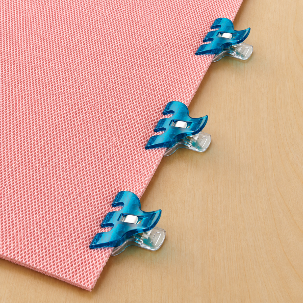 Three Clover Triple Wide Wonder Clips clipped along the diagonal edge of a pink nonwoven stabilizer on a wood surface