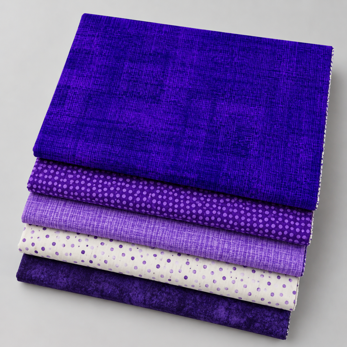 Interwoven Blueberry fabric layered with coordinating purple and cream quilting fabrics.