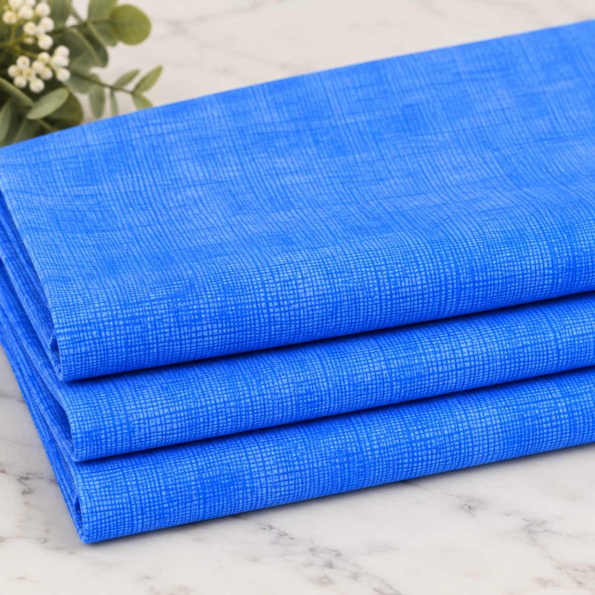 Interwoven Periwinkle Fabric by Jason Yenter for In The Beginning Fabrics — neatly folded fat quarter stack showing soft periwinkle blue-purple crosshatch tonal texture with fine linen-like woven grid pattern. Marble surface with white floral greenery. 100% cotton, 43–44" wide.