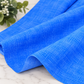 Interwoven Periwinkle Fabric by Jason Yenter for In The Beginning Fabrics — fabric draped and unfolded on a marble surface showing the fine crosshatch tonal texture with subtle lavender to cornflower blue tonal variation. White floral greenery in the corner. 100% cotton, 43–44" wide.