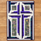 The Wondrous Cross handmade quilted wall décor with a white cross, purple and teal patchwork, and floral batik panels, laid flat on an oak floor.