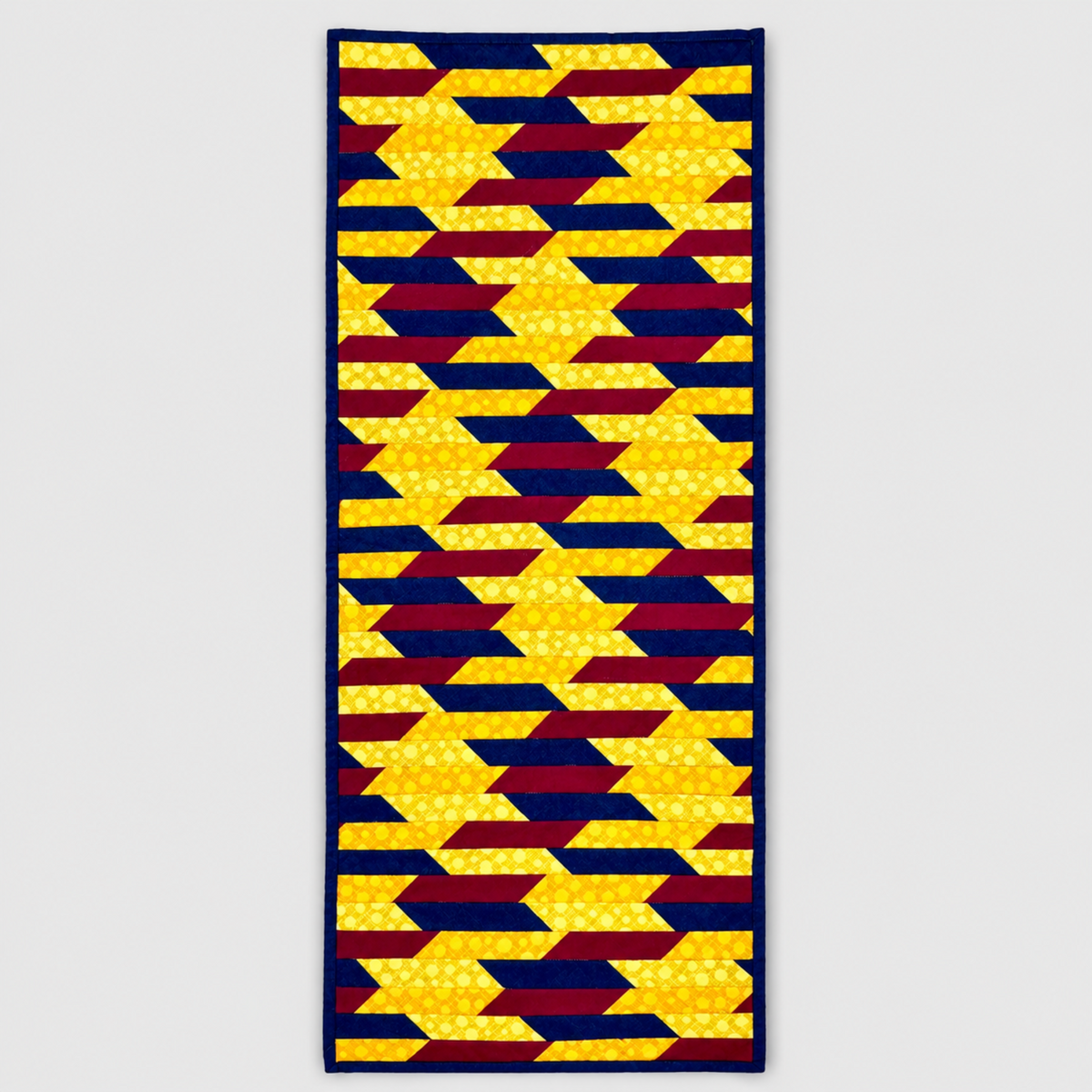 Golden Weave handmade quilted table runner with interlacing golden yellow, navy and burgundy strips, navy binding and straight ends on light gray.