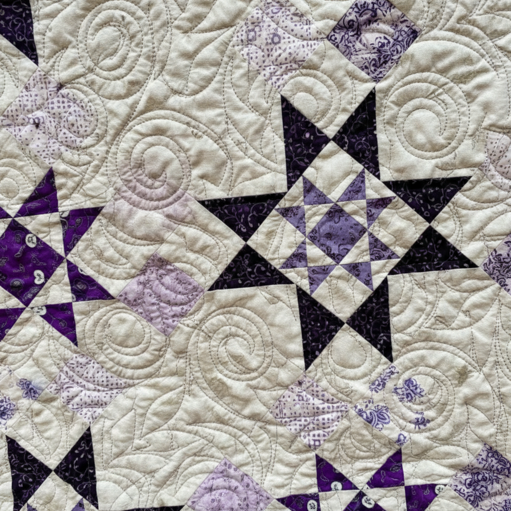 Close-up of purple star blocks and swirl quilting on handmade quilt