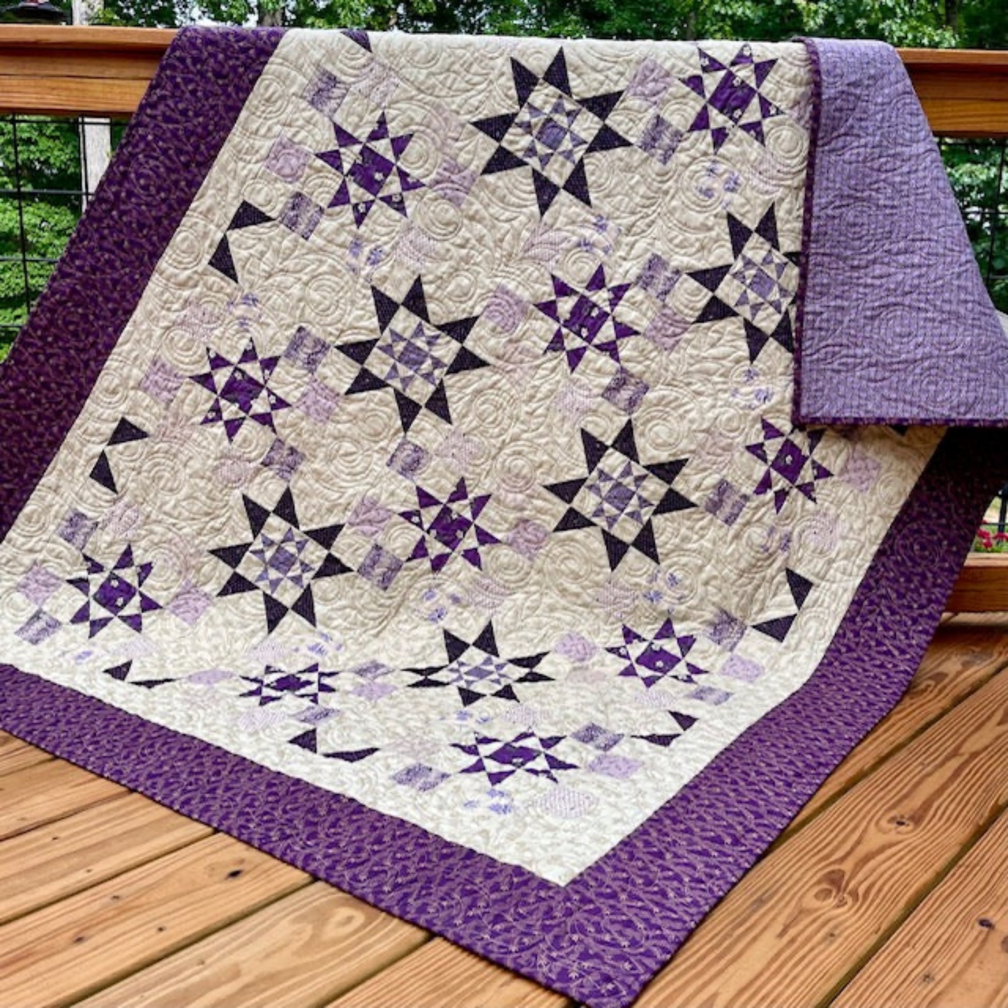 Purple star quilt draped over wooden deck railing in natural light