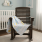 Wooden rocking chair with a baby quilt draped over it in a nursery setting.