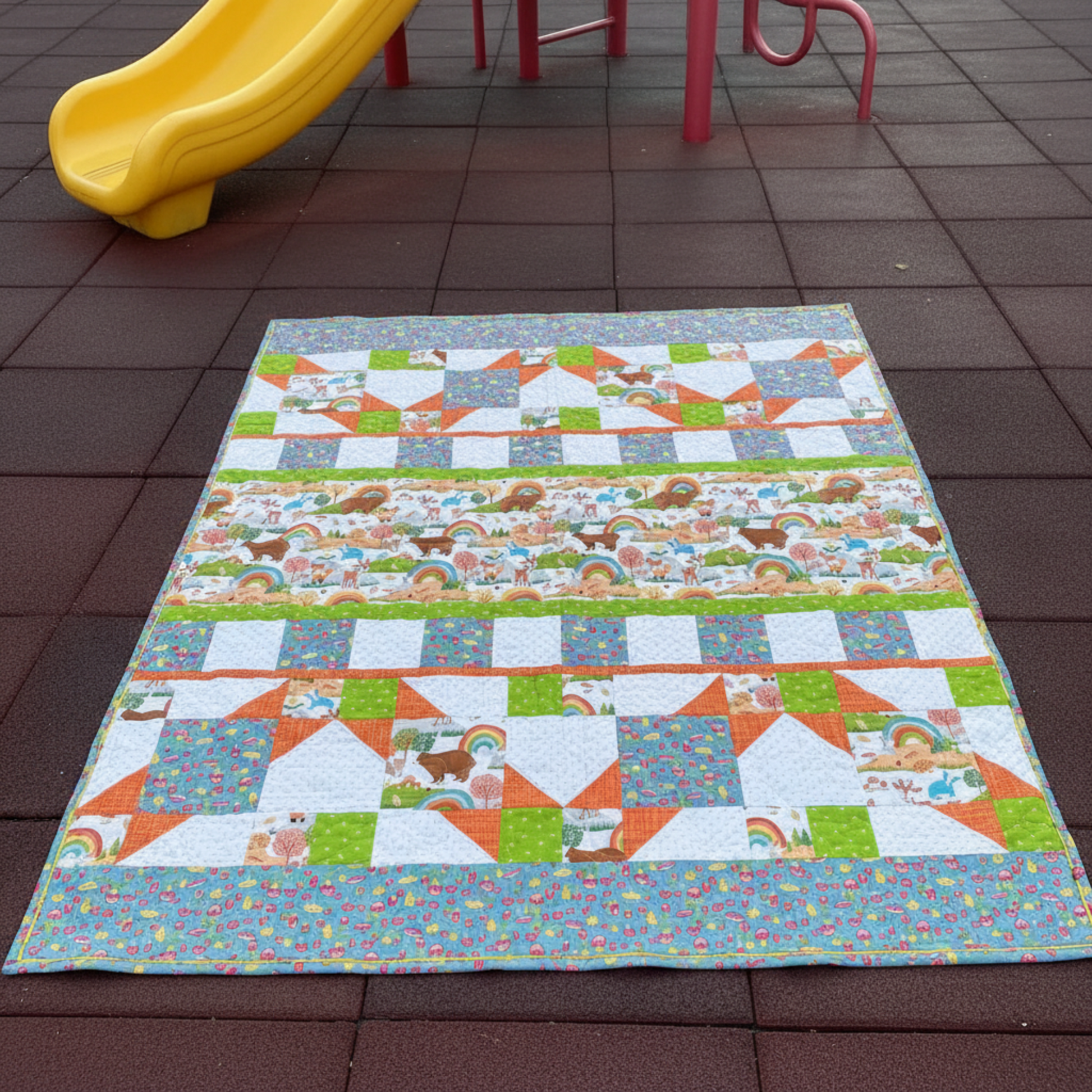 Colorful quilt with animal patterns on a tiled floor with a yellow slide in the background