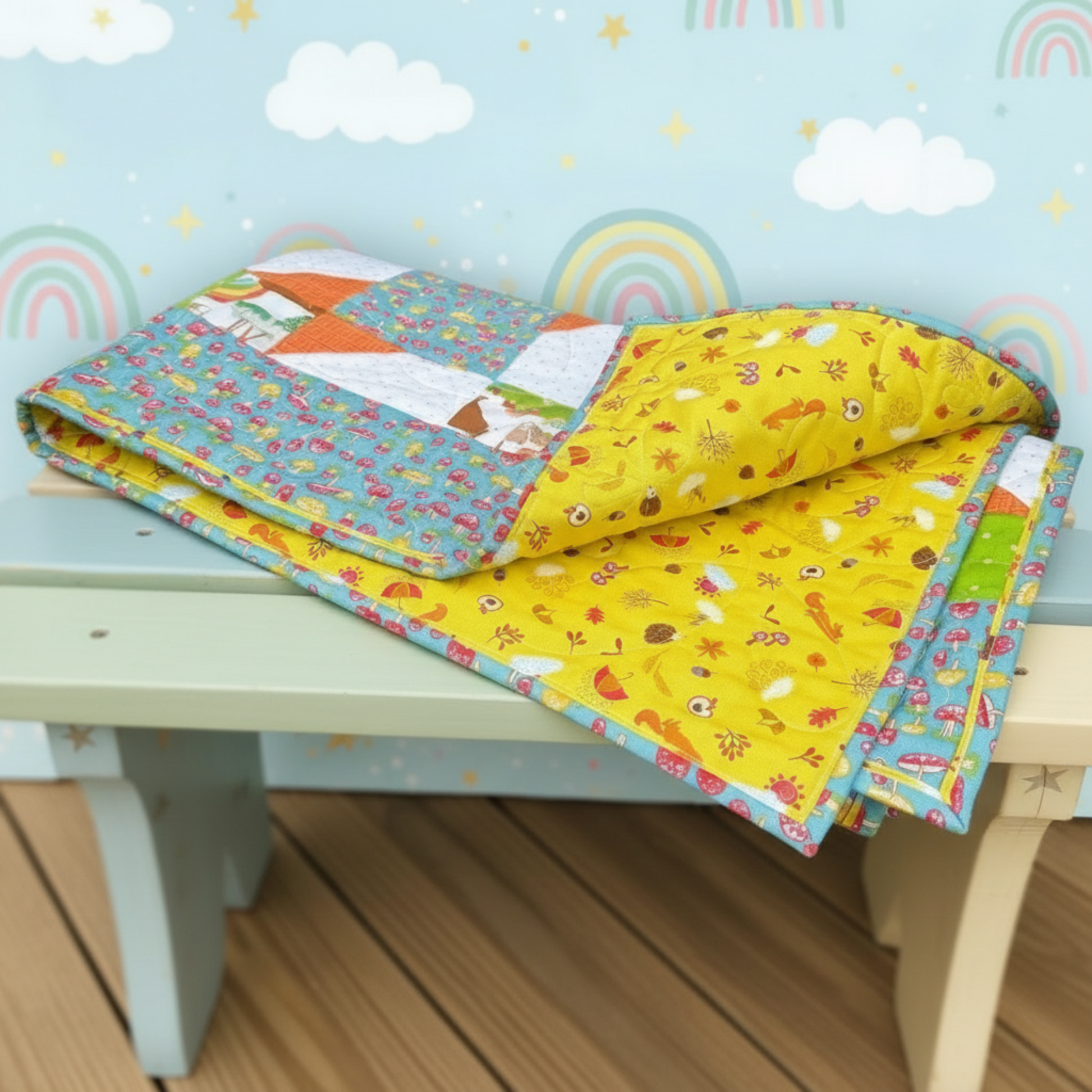 Colorful quilt with animal patterns on a light blue table against a wall with rainbow and cloud decorations.