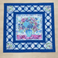 Handmade floral quilt featuring a blue and purple flower arrangement in a vase, framed by layered blue borders.