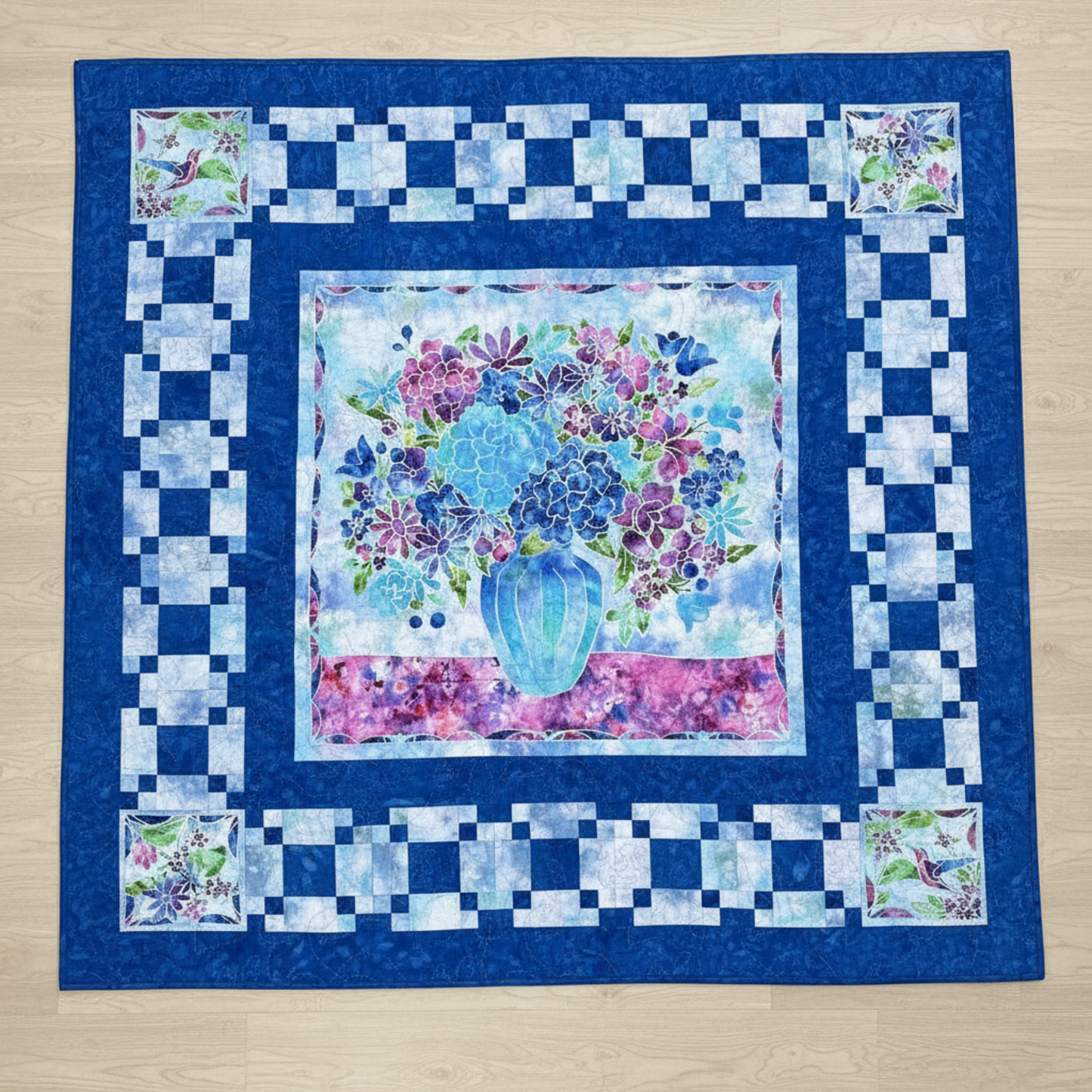 Handmade floral quilt featuring a blue and purple flower arrangement in a vase, framed by layered blue borders.