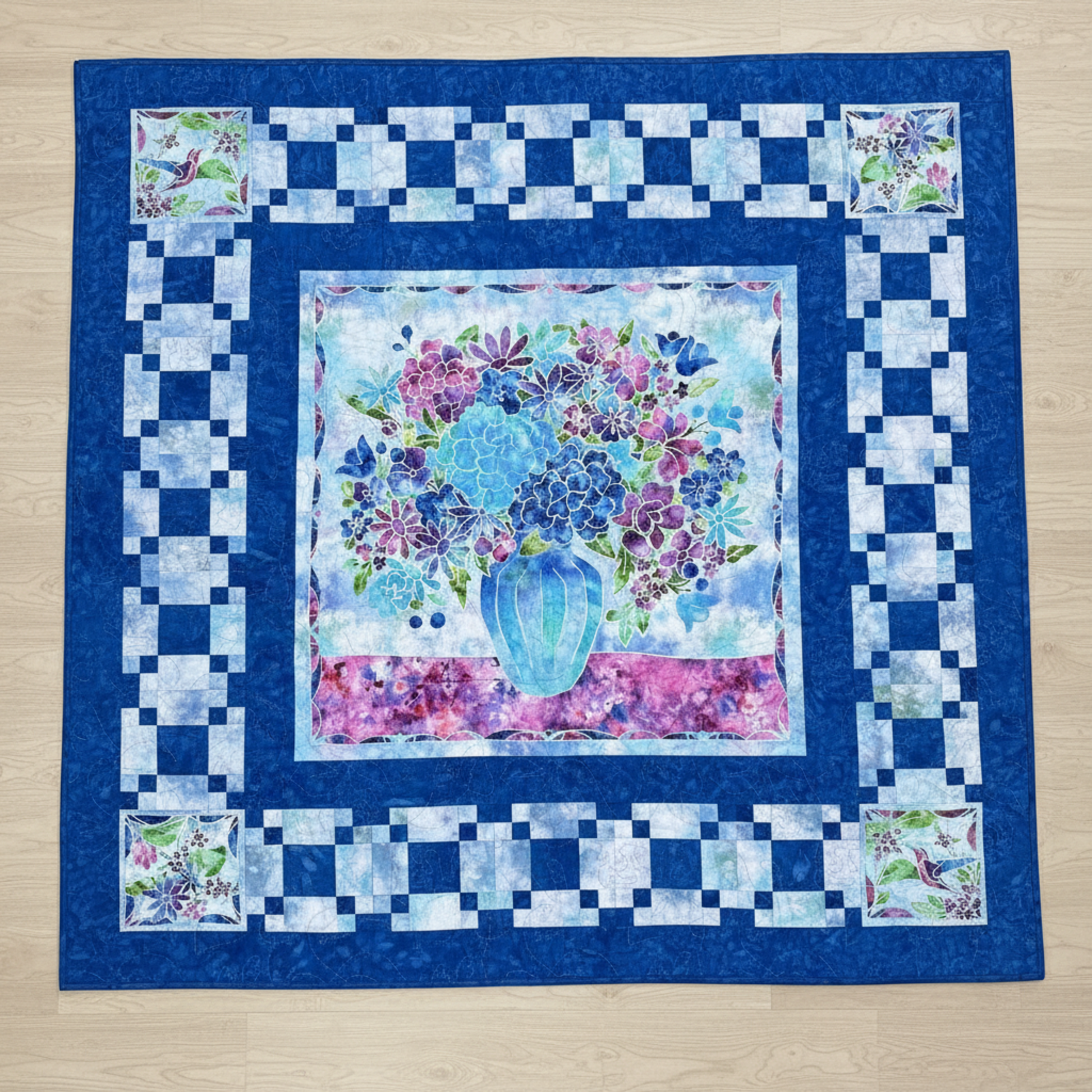 Handmade floral quilt featuring a blue and purple flower arrangement in a vase, framed by layered blue borders.