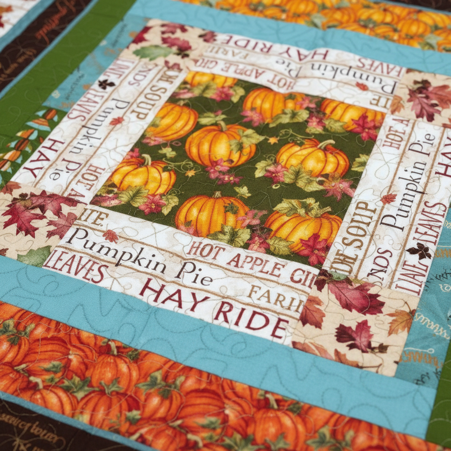 Close-up of handmade autumn quilt showing pumpkin fabric, fall leaves, and harvest-themed text.