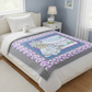 Bed with a colorful quilt featuring cartoon characters, white teddy bear, and nightstand with lamp.