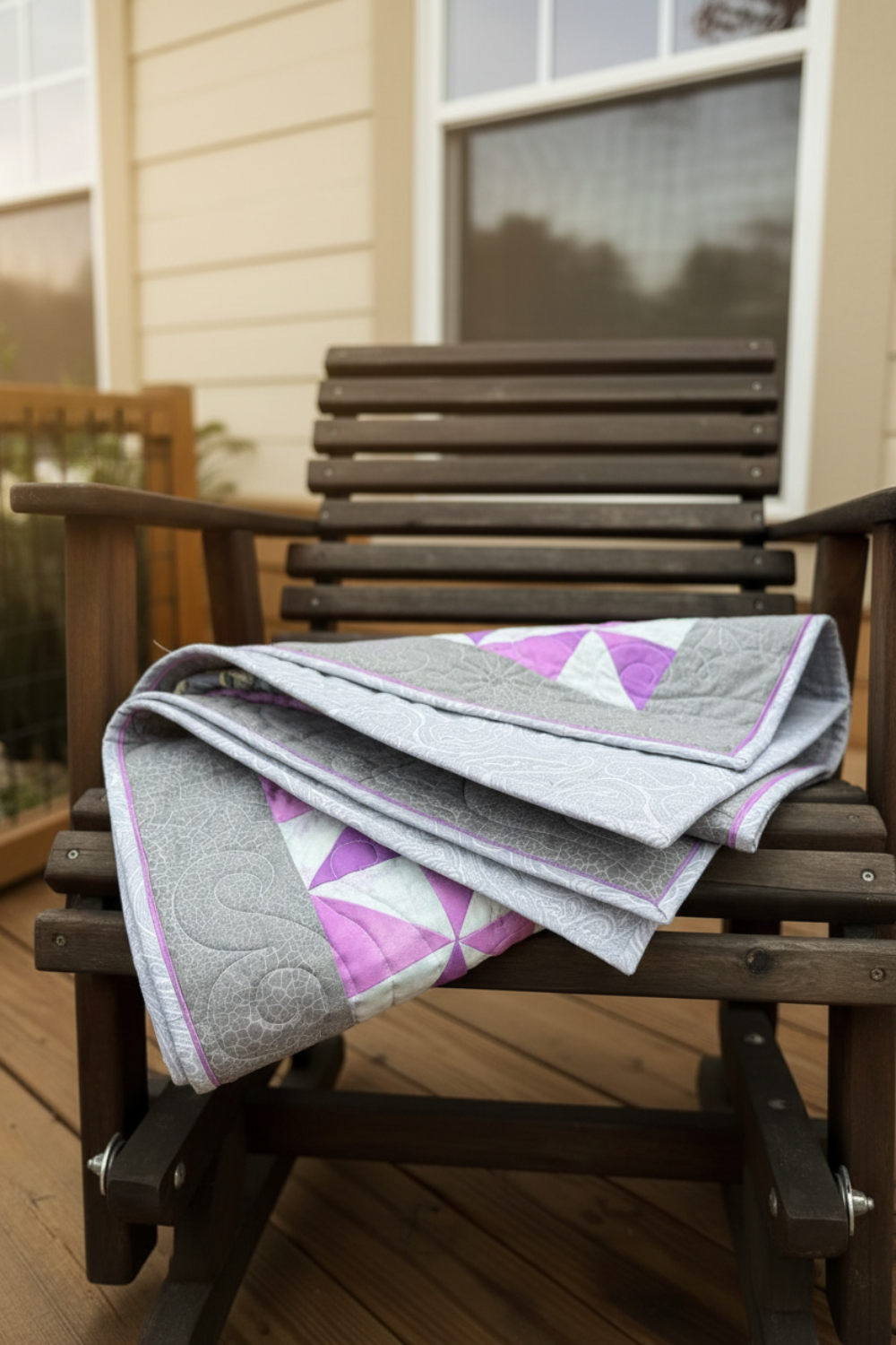 Quilt with pink triangles draped over a wooden chair on a deck.