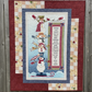 Quilt with snowman design and text on a wooden surface