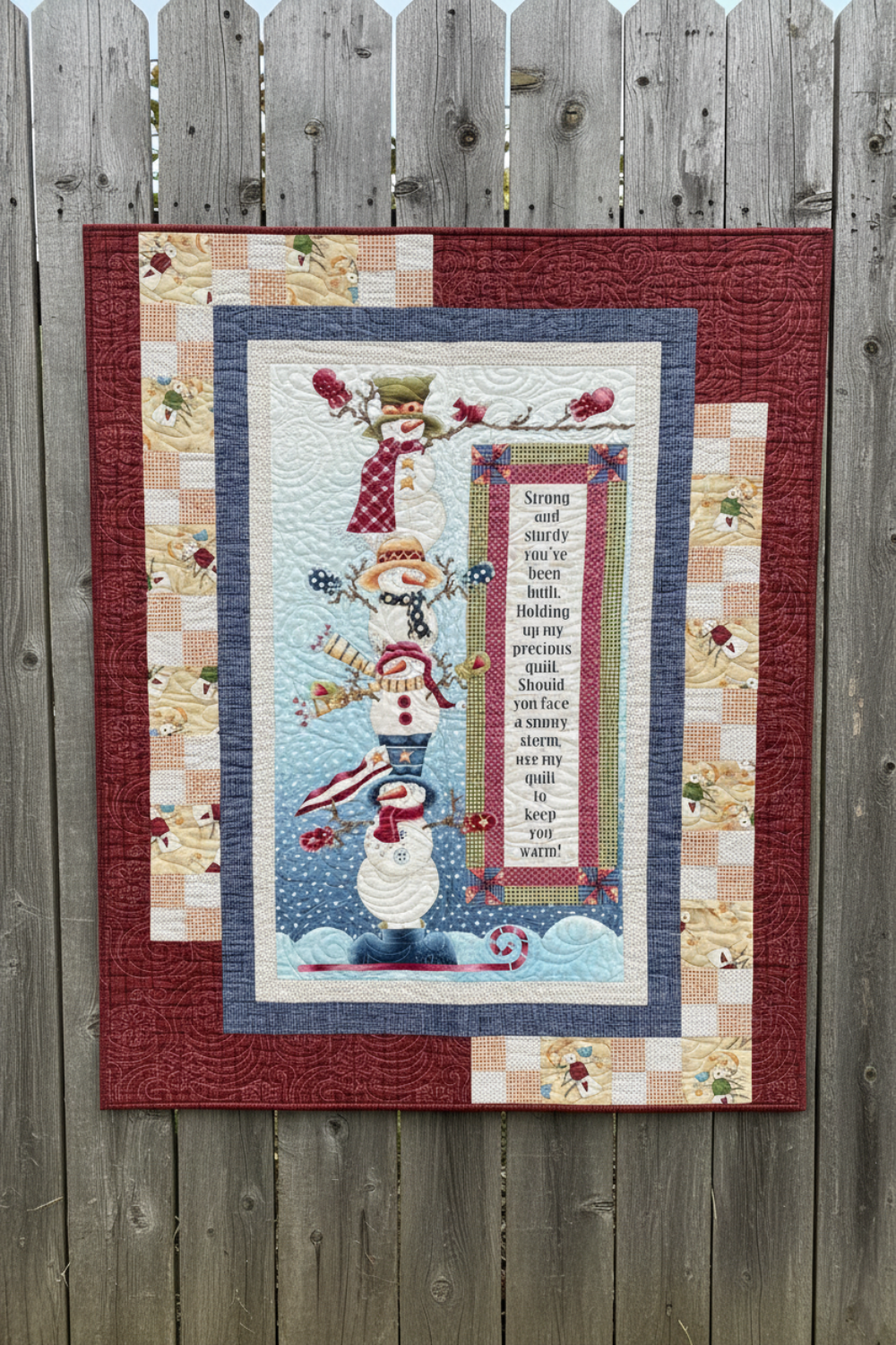 Quilt with snowman design and text on a wooden surface