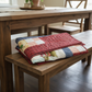 Quilted patchwork blanket on a wooden bench in a dining room setting